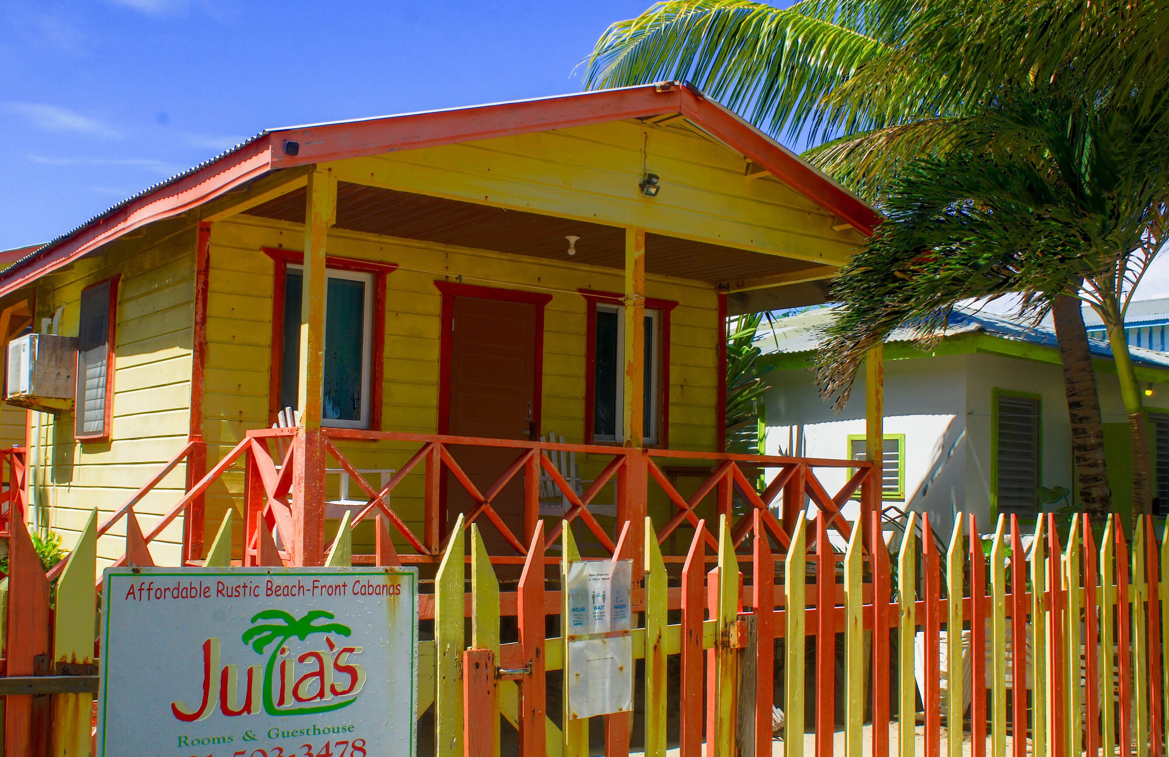 Un edificio amarillo con detalles rojos, un letrero que dice Julia's Rooms & Guesthouse, y una cerca roja y amarilla.