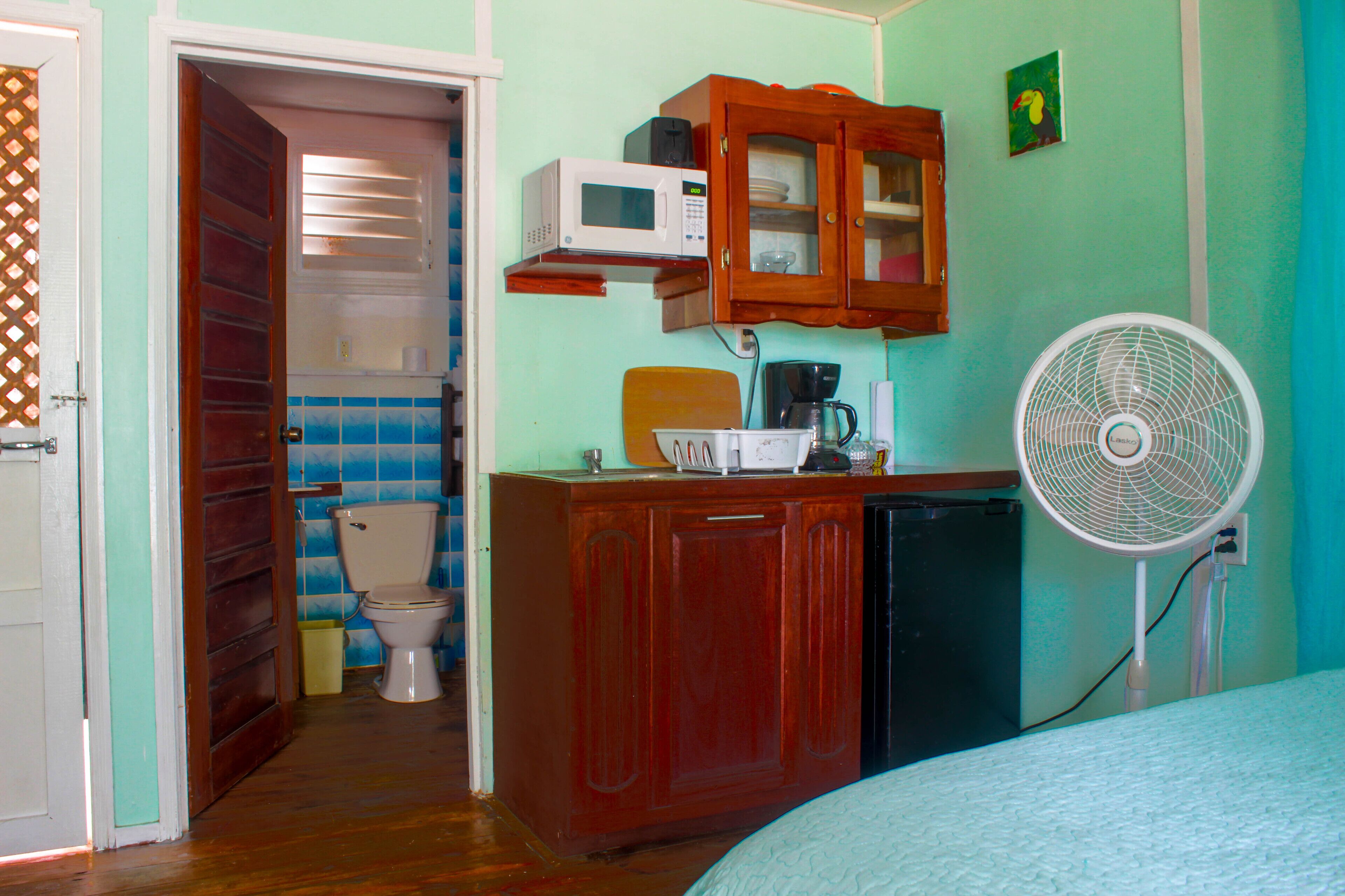 Ein kleines Zimmer mit einem Holzkästen, einer Mikrowelle, einem Ventilator und einer Toilette.
