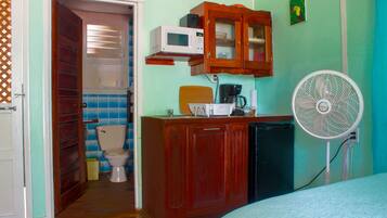 Ein kleines Zimmer mit einem Holzkästen, einer Mikrowelle, einem Ventilator und einer Toilette.