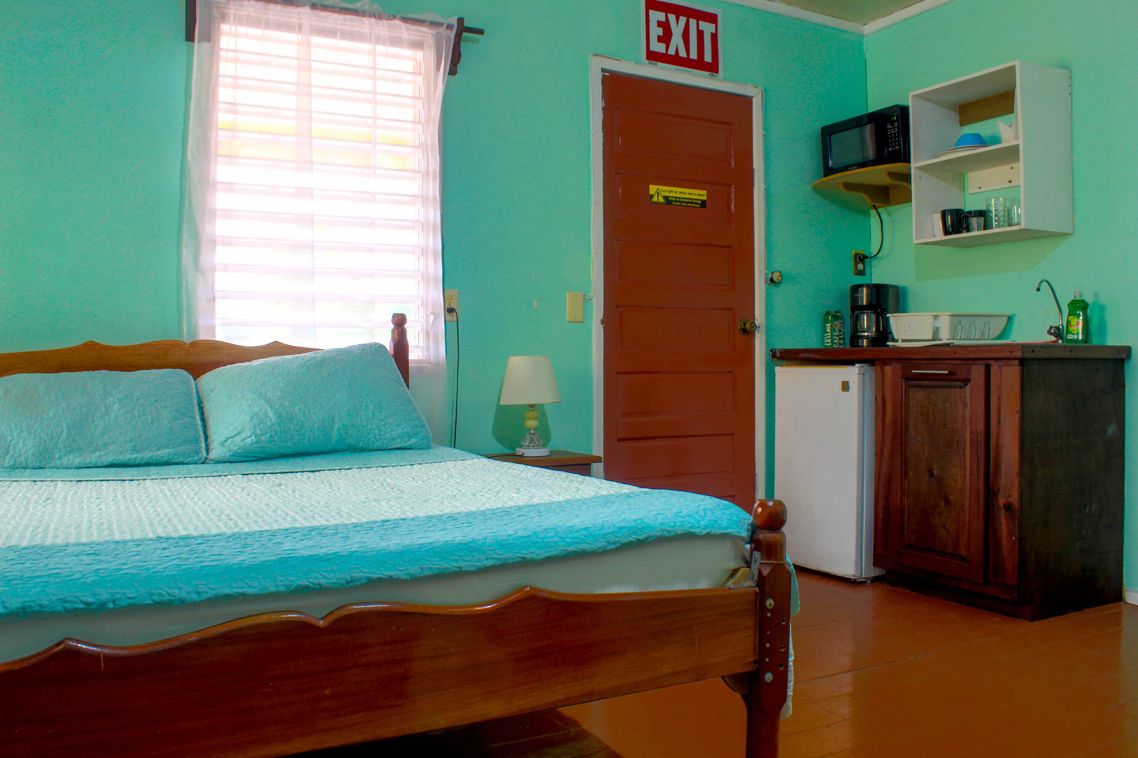 A bedroom with a bed, an exit sign, a microwave, a coffee maker, and a small cabinet.