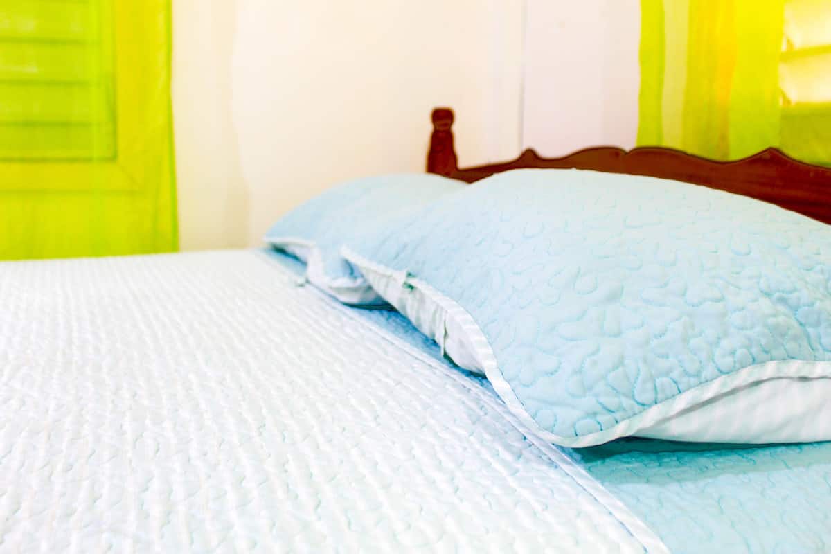A bed with a quilted blue blanket and a matching pillow.