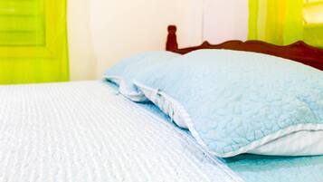 A bed with a quilted blue blanket and a matching pillow.
