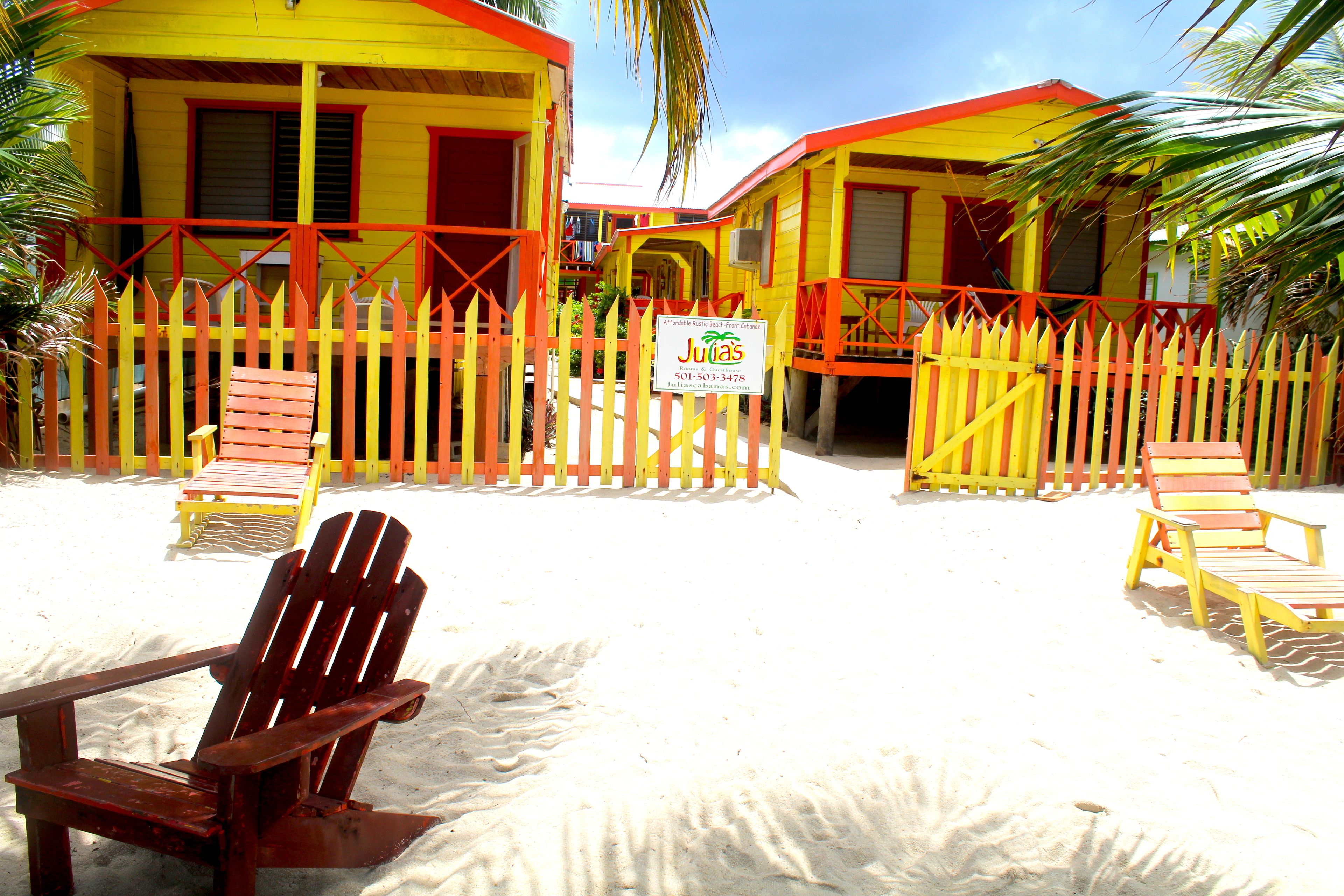 A beachside property with two yellow buildings, a wooden fence, and beach chairs.