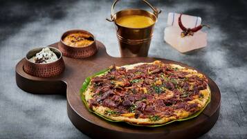 Una pizza sobre una tabla de madera con una olla de metal y dos recipientes pequeños a un lado.