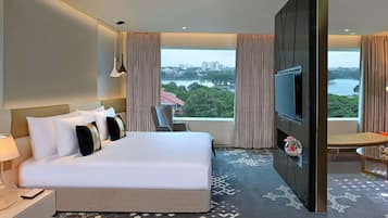 A hotel room with a large bed, a TV, a desk, and a view of a cityscape and water.