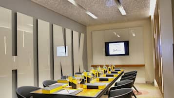 Un salón de conferencias con una larga mesa, sillas y una pantalla de televisión que muestra un mensaje de bienvenida.