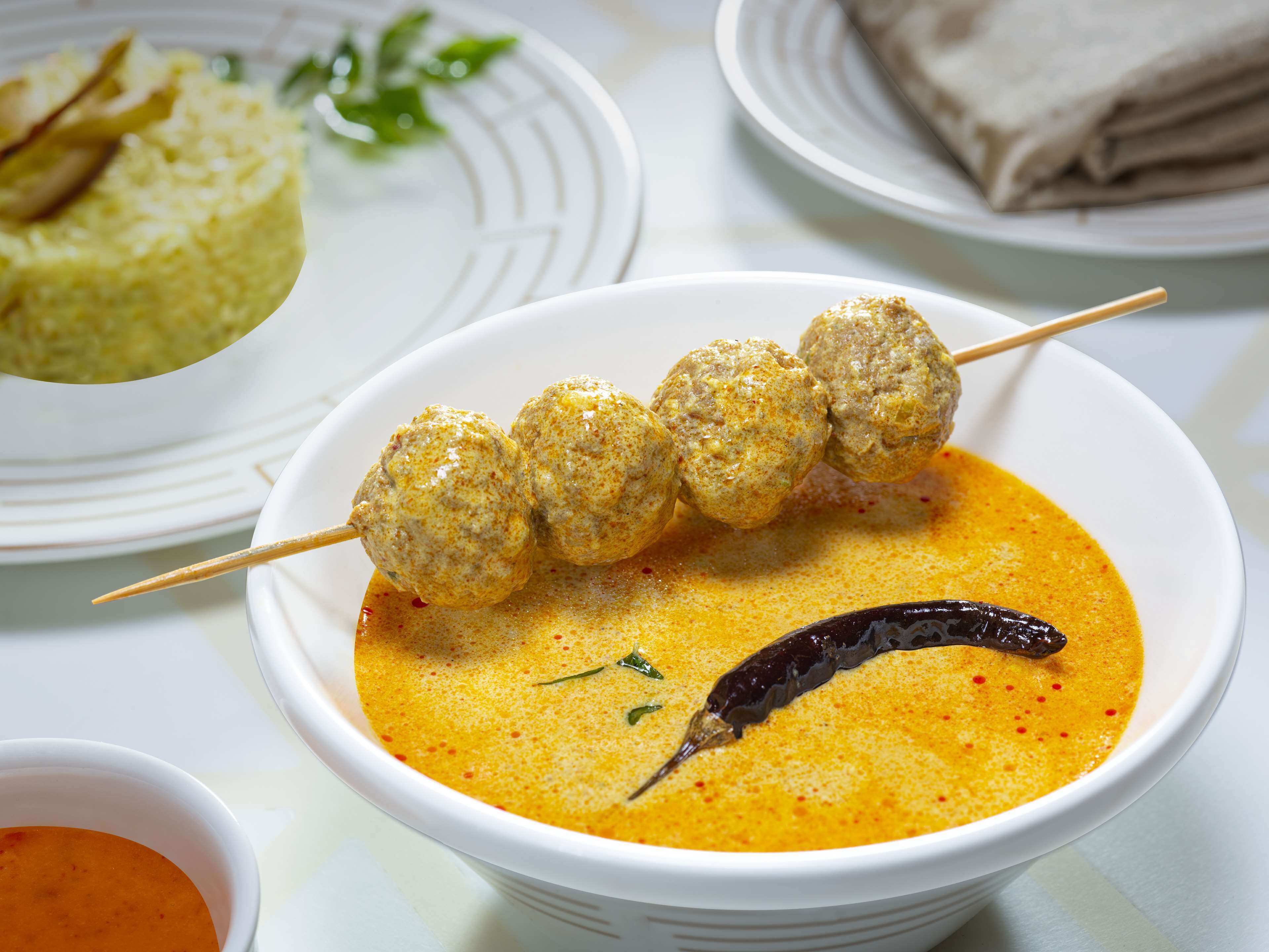 A bowl of soup with meatballs and a chili pepper garnish.