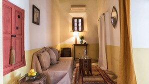 A narrow hallway with a bed, a small table with a lamp, and a red door. - Riad Sasha (Marrakech)