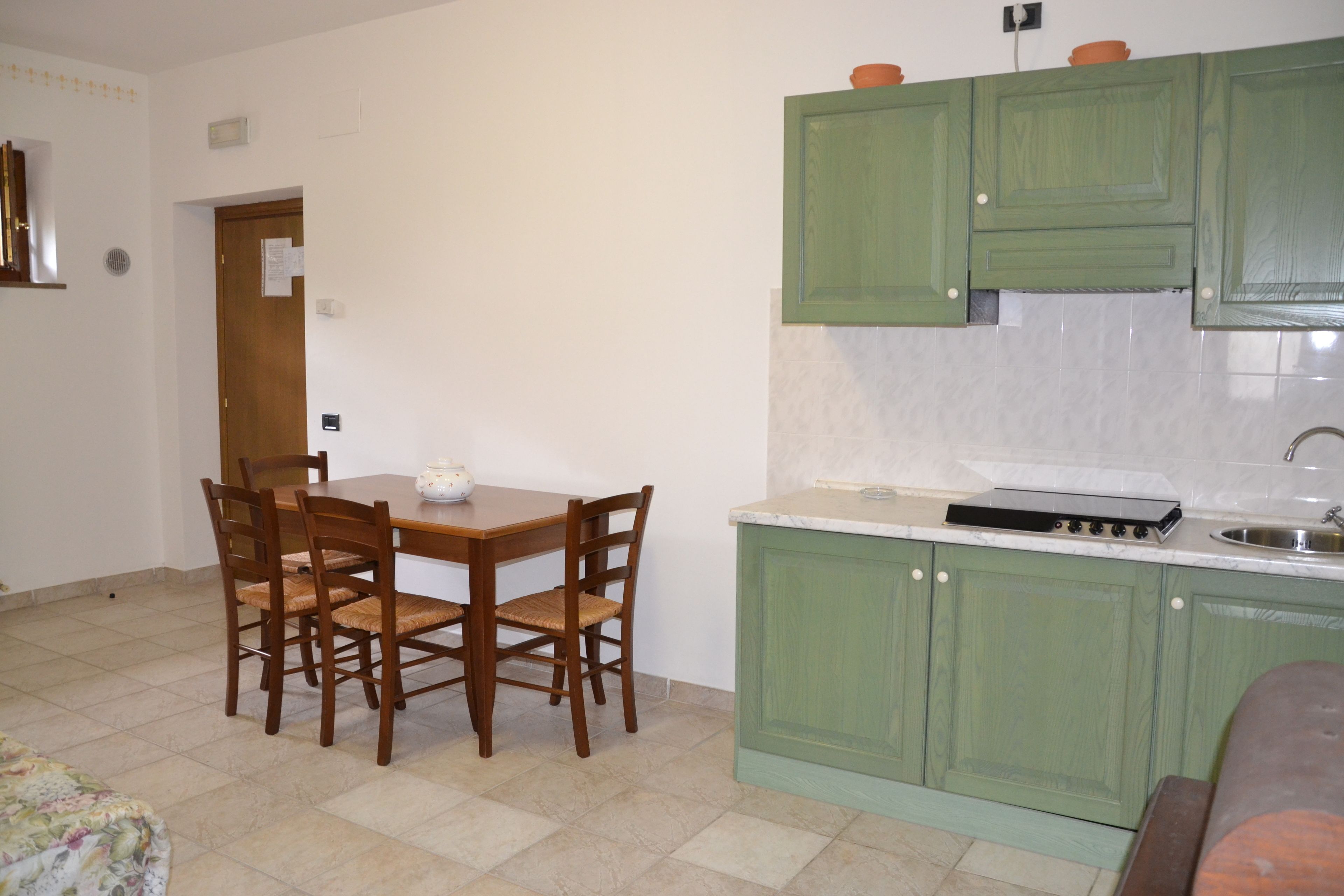 Une cuisine avec des meubles de couleur verte, une table à manger avec des chaises et un plan de travail avec un évier.