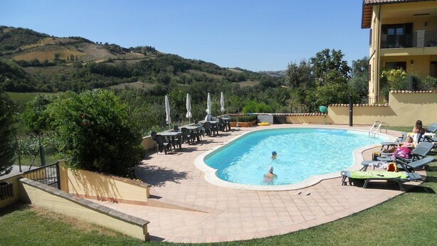 A swimming pool with a view of hills, outdoor seating, and a building with a balcony. - Agriturismo La Selva (Nocera Umbra)