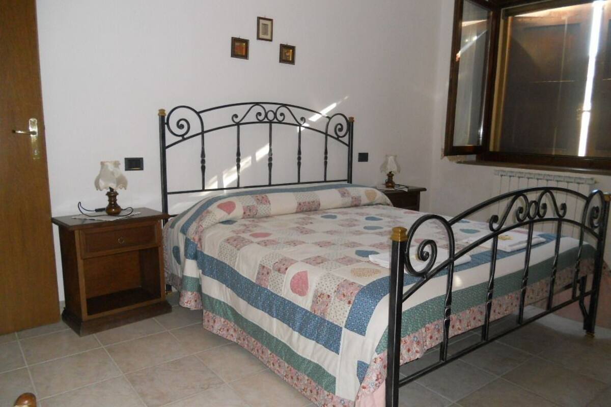 A bedroom with a metal bed frame, a bedside table with a lamp, and a window with blinds.