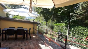 An outdoor patio with a table and chairs under a canopy, surrounded by greenery and a railing. - Agriturismo La Selva (Nocera Umbra)