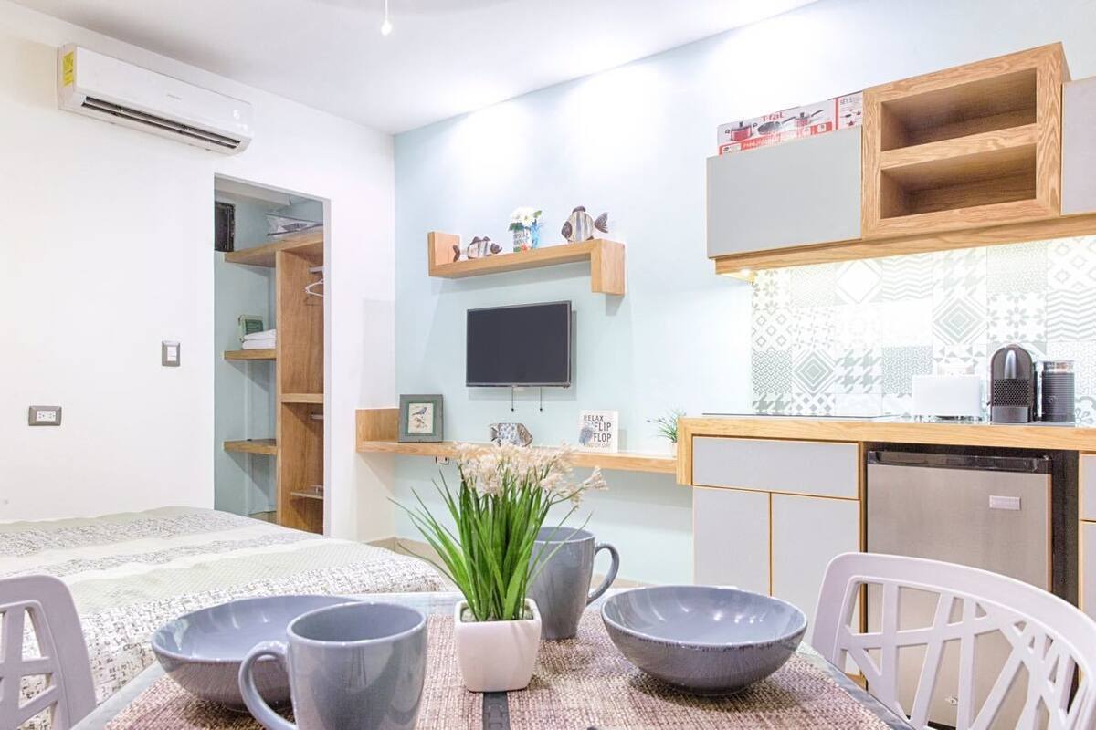 A modern kitchen with a built-in TV, wooden shelves, and a dining area with a table set for two.