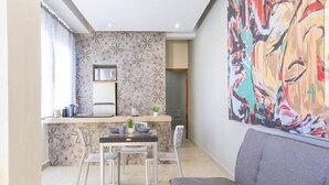 A compact living space with a kitchenette, a dining area, and a large abstract painting. - Suites Calle 8 (Playa del Carmen)