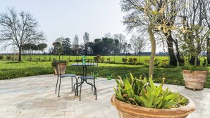 An outdoor patio with a table and chairs, surrounded by potted plants and a view of a green field. - Villa Archi (Faenza)