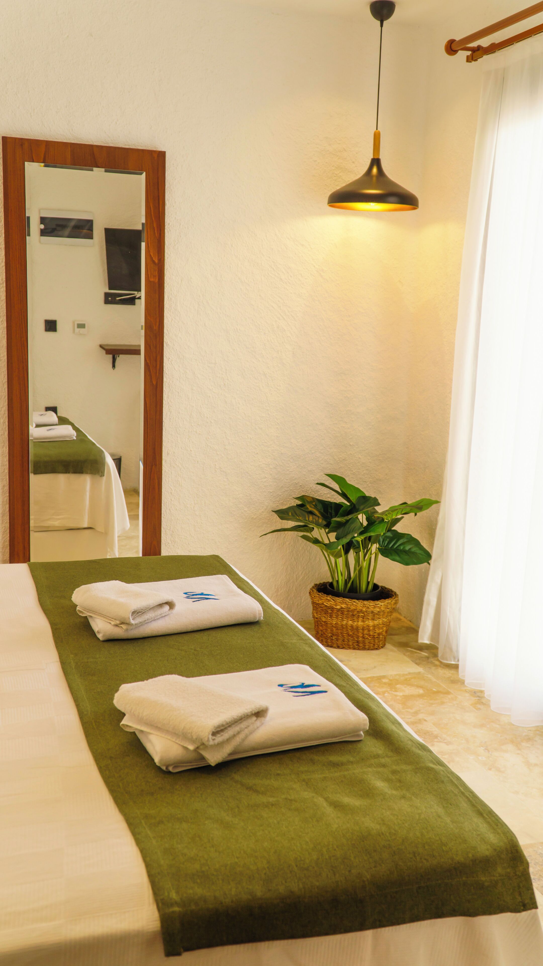 Een hotelkamer met een bed, een groene handdoek, een plant en een spiegel.