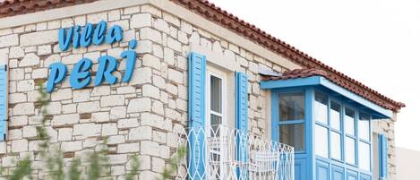 Un edificio con fachada de piedra y contraventanas azules, identificado como "villa perj".