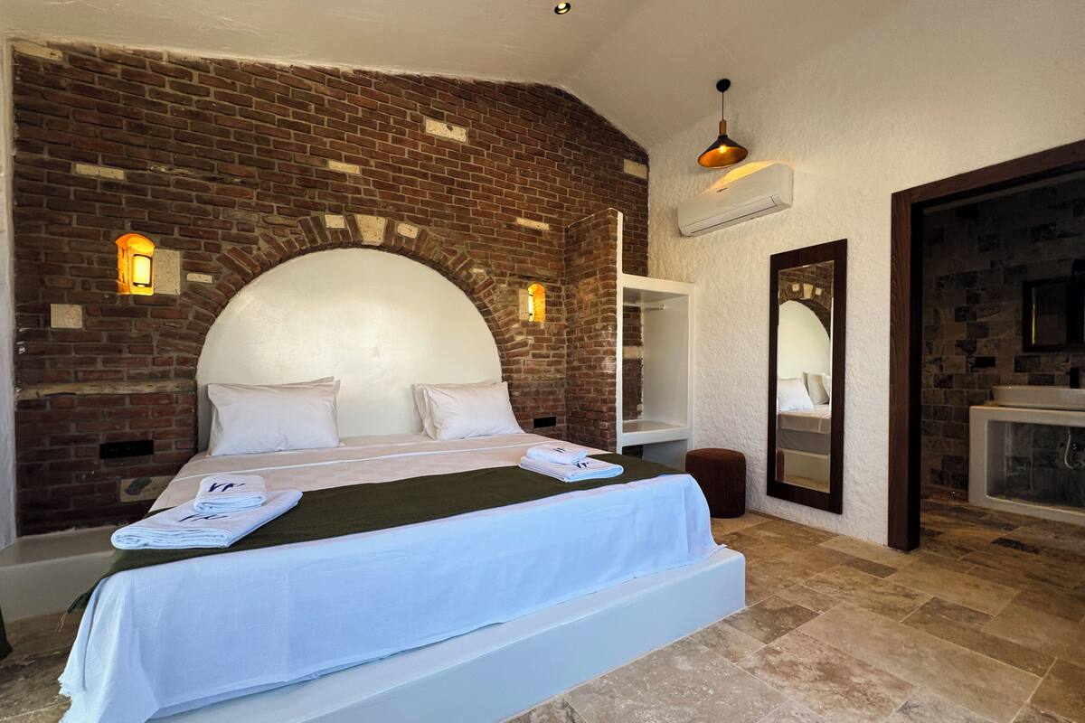 Un dormitorio con pared de ladrillo, una cama grande, un espejo y un baño con bañera.