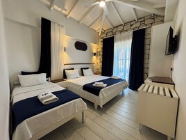 Habitación de hotel con dos camas, una pared decorativa de piedra, un ventilador de techo y un televisor montado en la pared.