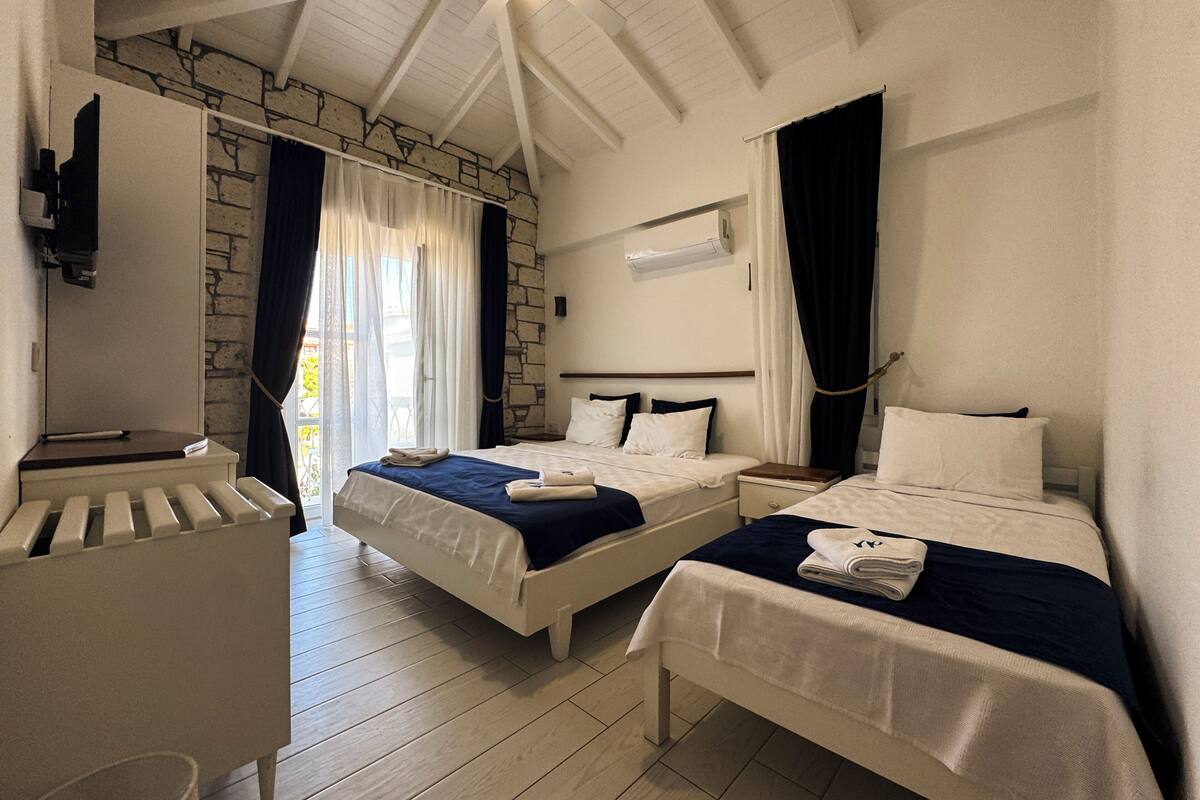 Habitación de hotel con dos camas, piso de madera, pared de piedra y ventilador de techo.