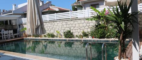 A pool area with lounge chairs and umbrellas, surrounded by a stone wall and potted plants.