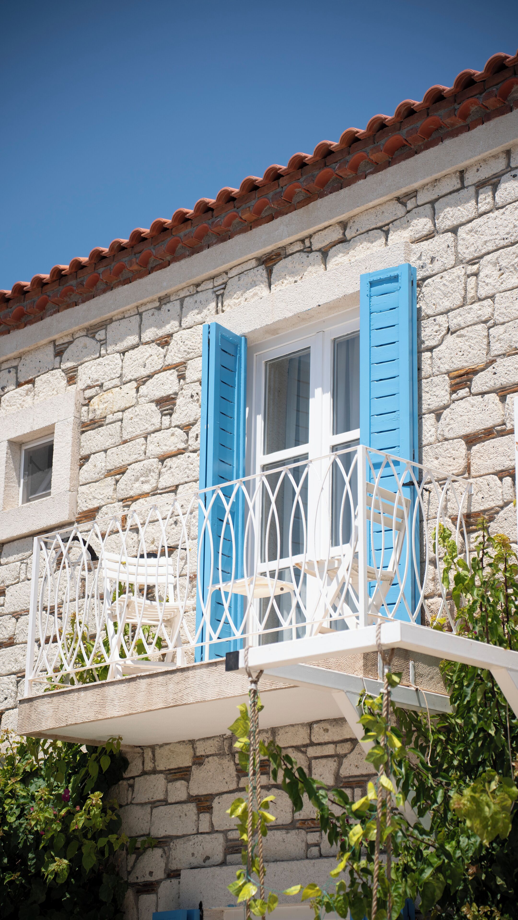 Ein Steinhaus mit Balkon, blauen Fensterläden und einem weißen Geländer.