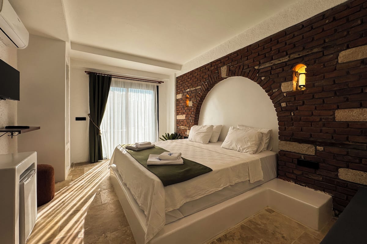 Un dormitorio moderno con una pared de ladrillo decorativa, una cama grande con ropa de cama blanca, un banco empotrado y un televisor de pantalla plana en un estante.