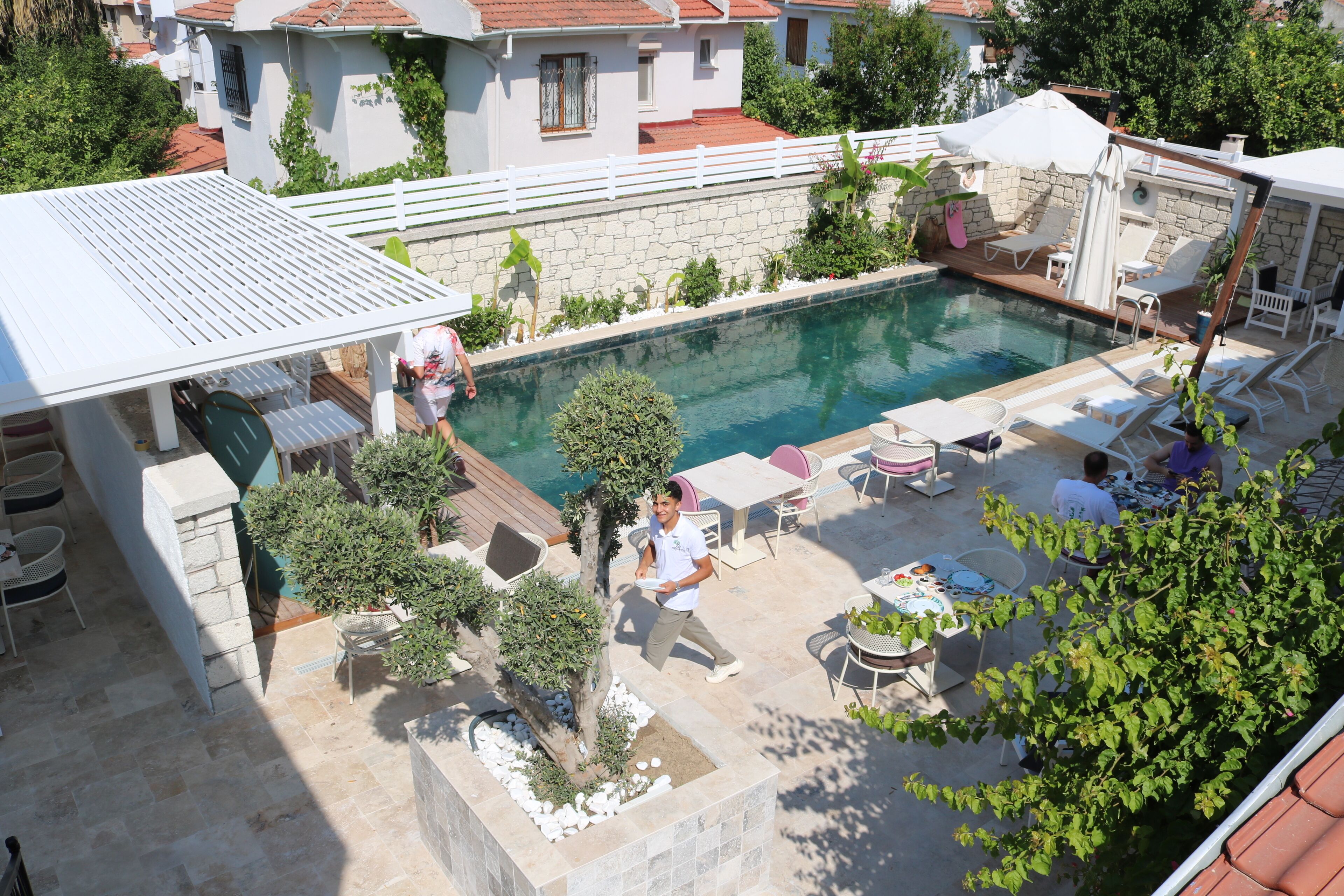 Ein Poolbereich mit Steinplatten, Liegestühlen und einer überdachten Sitzgelegenheit.