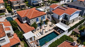 An aerial view of a residential area with a swimming pool, stone buildings, and red-tiled roofs. - Villa Peri Alacati (Cesme)
