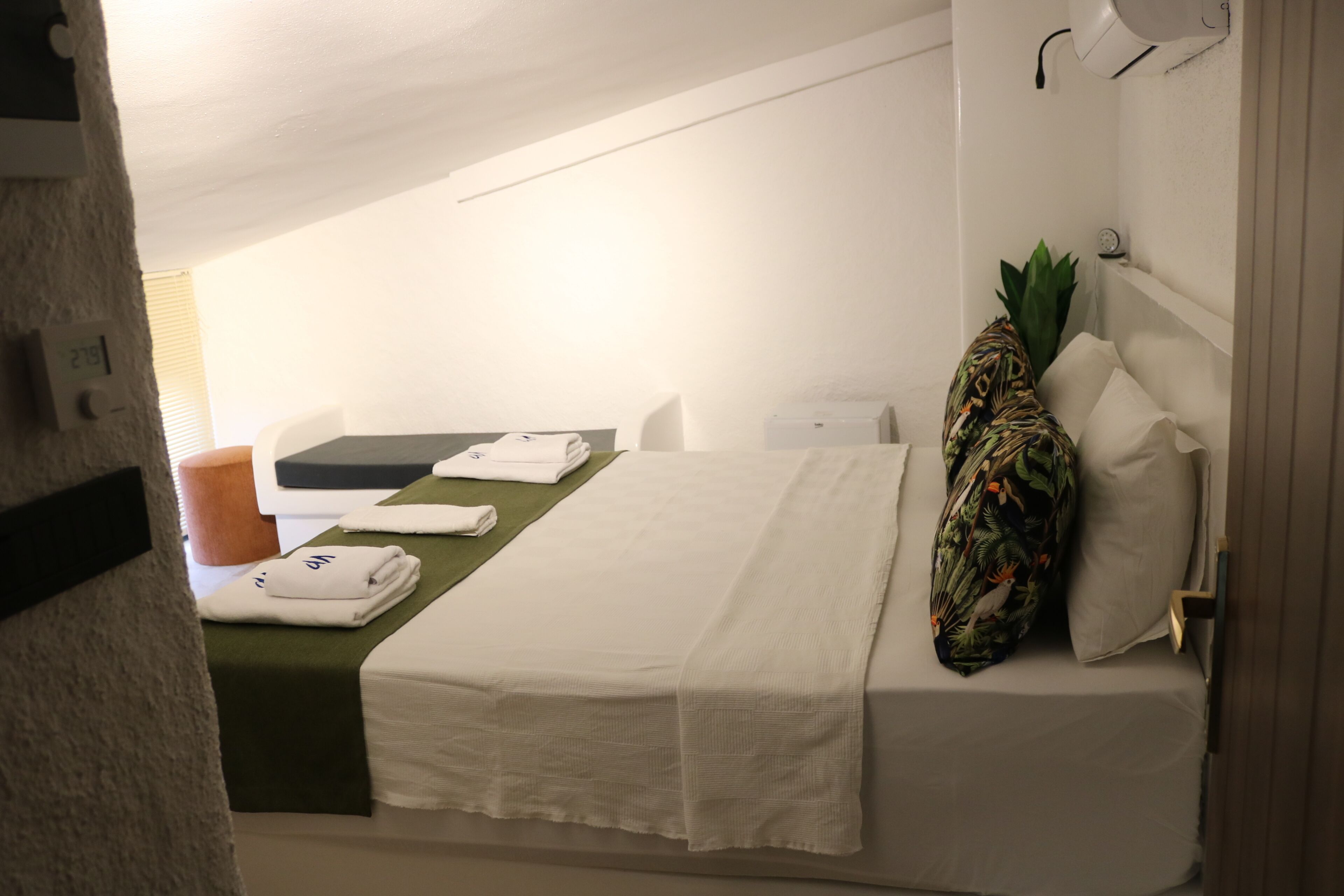 A hotel room with a bed, a desk, a chair, a small table, and a plant.