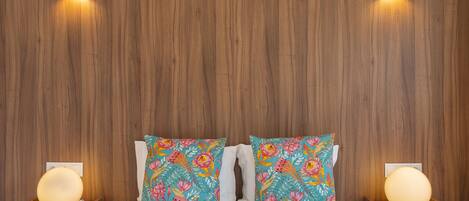 A hotel room with a wooden headboard, two bedside tables with lamps, and floral-patterned pillows.