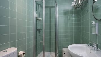 Un baño con ducha envuelta en vidrio, inodoro, lavamanos y perchero para toallas.