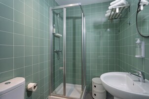 Un baño con ducha envuelta en vidrio, inodoro, lavamanos y perchero para toallas.