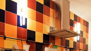 A kitchen with a checkered backsplash, stainless steel appliances, and open shelving with dishes and cookware.
