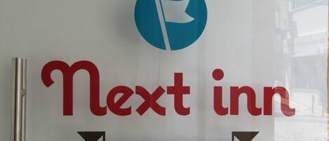 A sign for Next inn with a logo and the text 'BUDGET ACCOMODATION'.