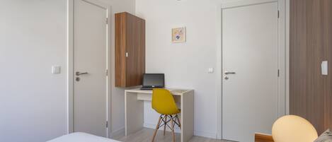 A bedroom with a bed, a desk with a laptop, a yellow chair, and a wardrobe.