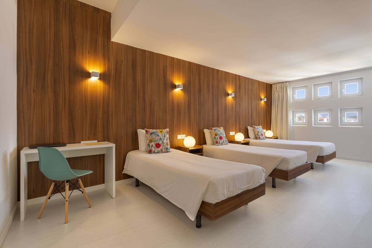 Quarto de hotel com duas camas, uma escrivaninha e uma cadeira.