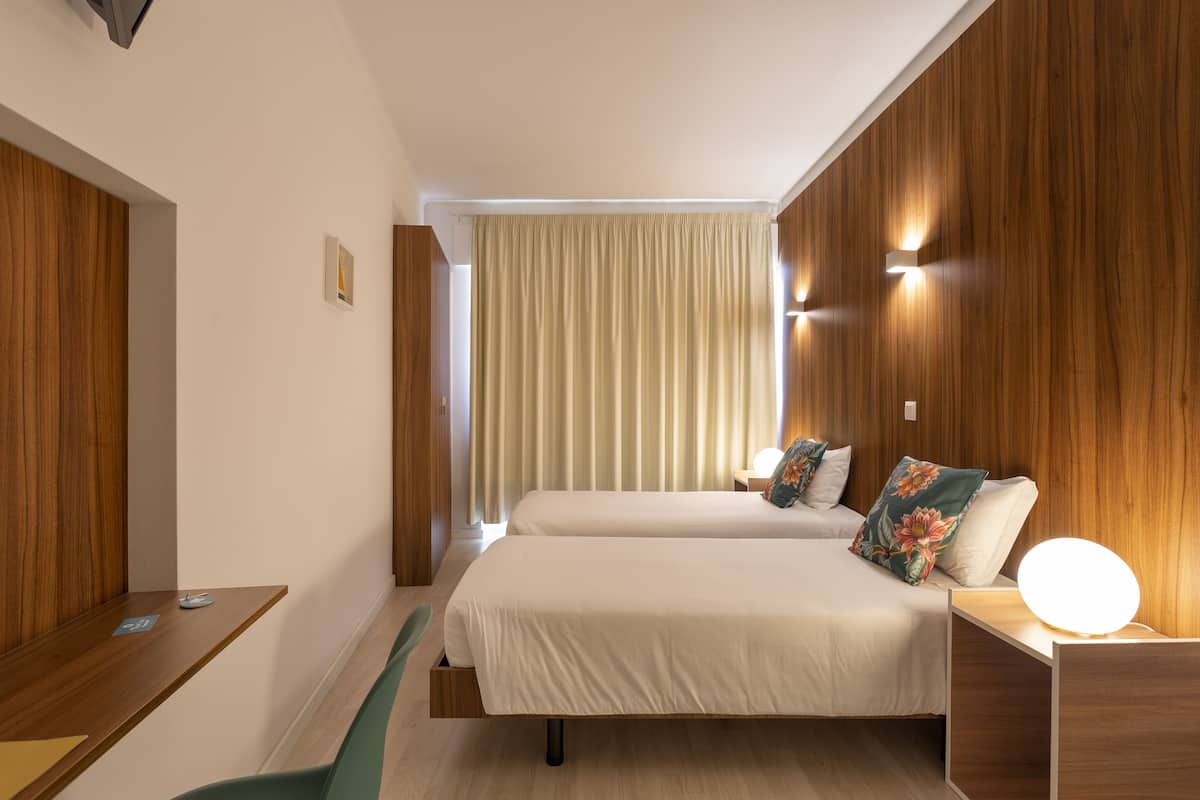 Quarto de hotel com duas camas, uma escrivaninha e uma cadeira.