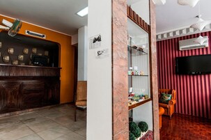 Zona de recepción con mostrador de madera, área de asientos con una silla, un pilar de mármol y un televisor montado en una pared a rayas.