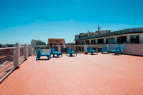 Una terraza en la azotea con sillas de plástico azul y una valla de metal.