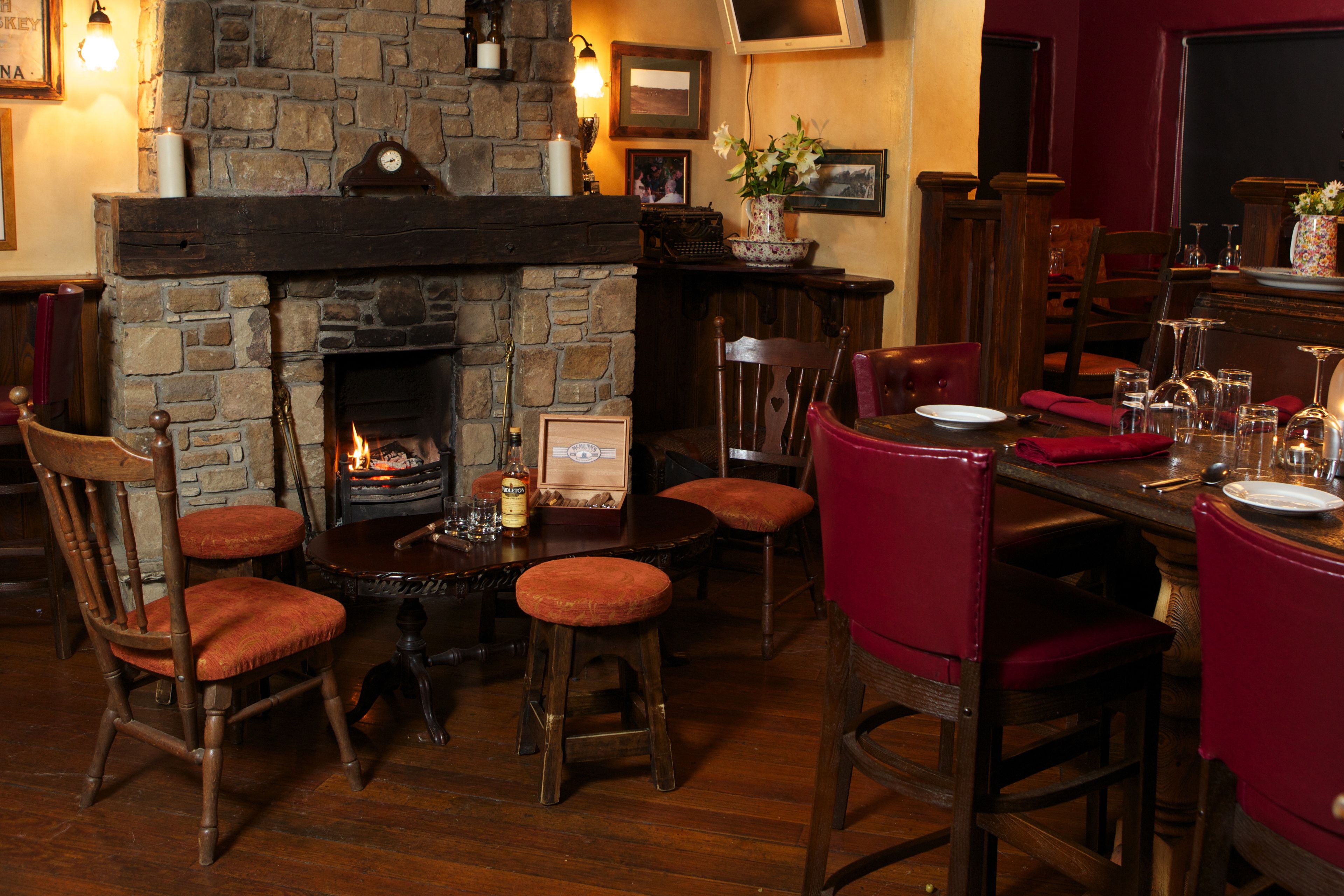 A cozy pub with a stone fireplace, wooden furniture, and a television mounted on the wall.