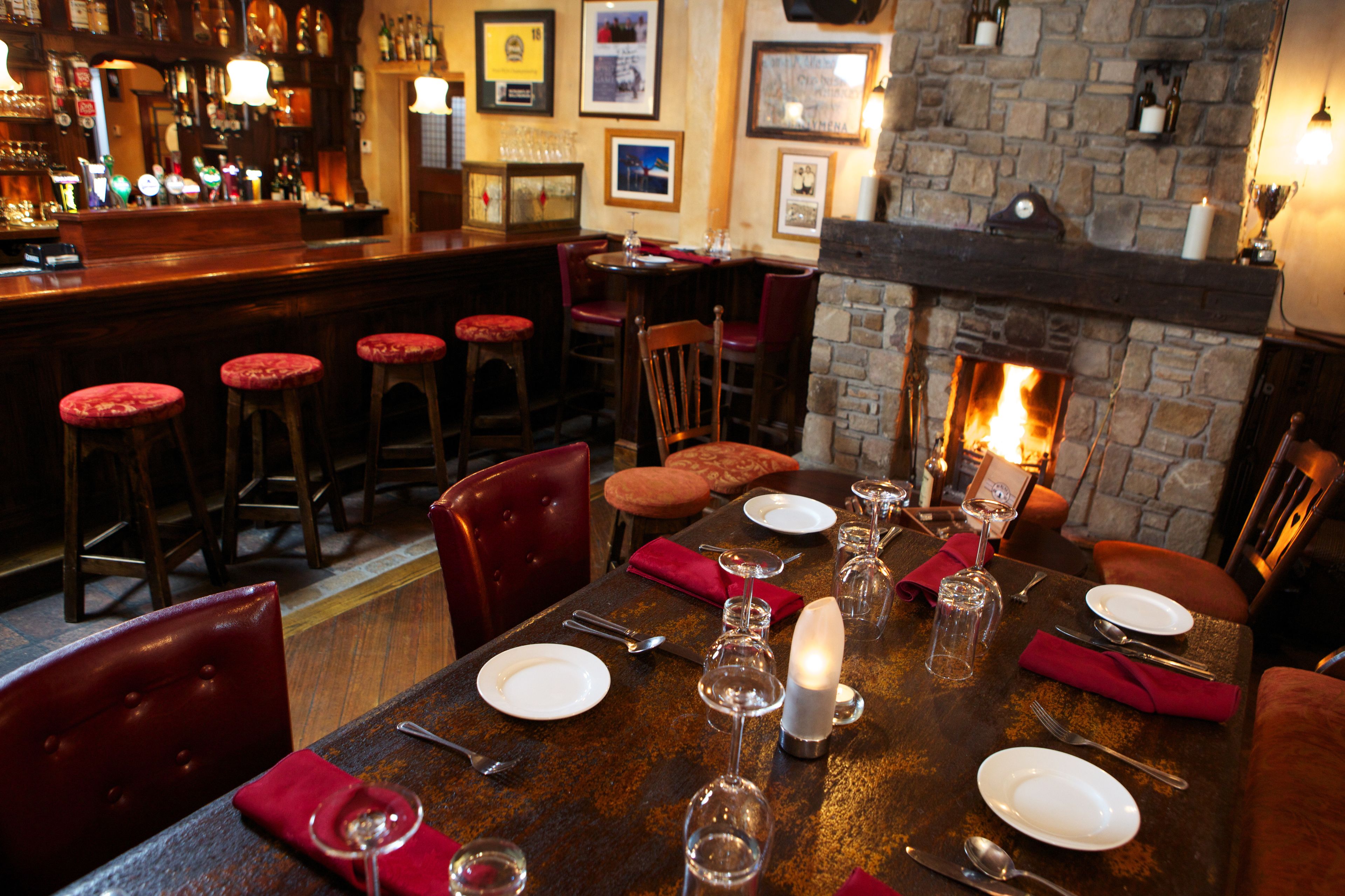 A bar area with stools, a fireplace, and a dining table set with plates, glasses, and cutlery.