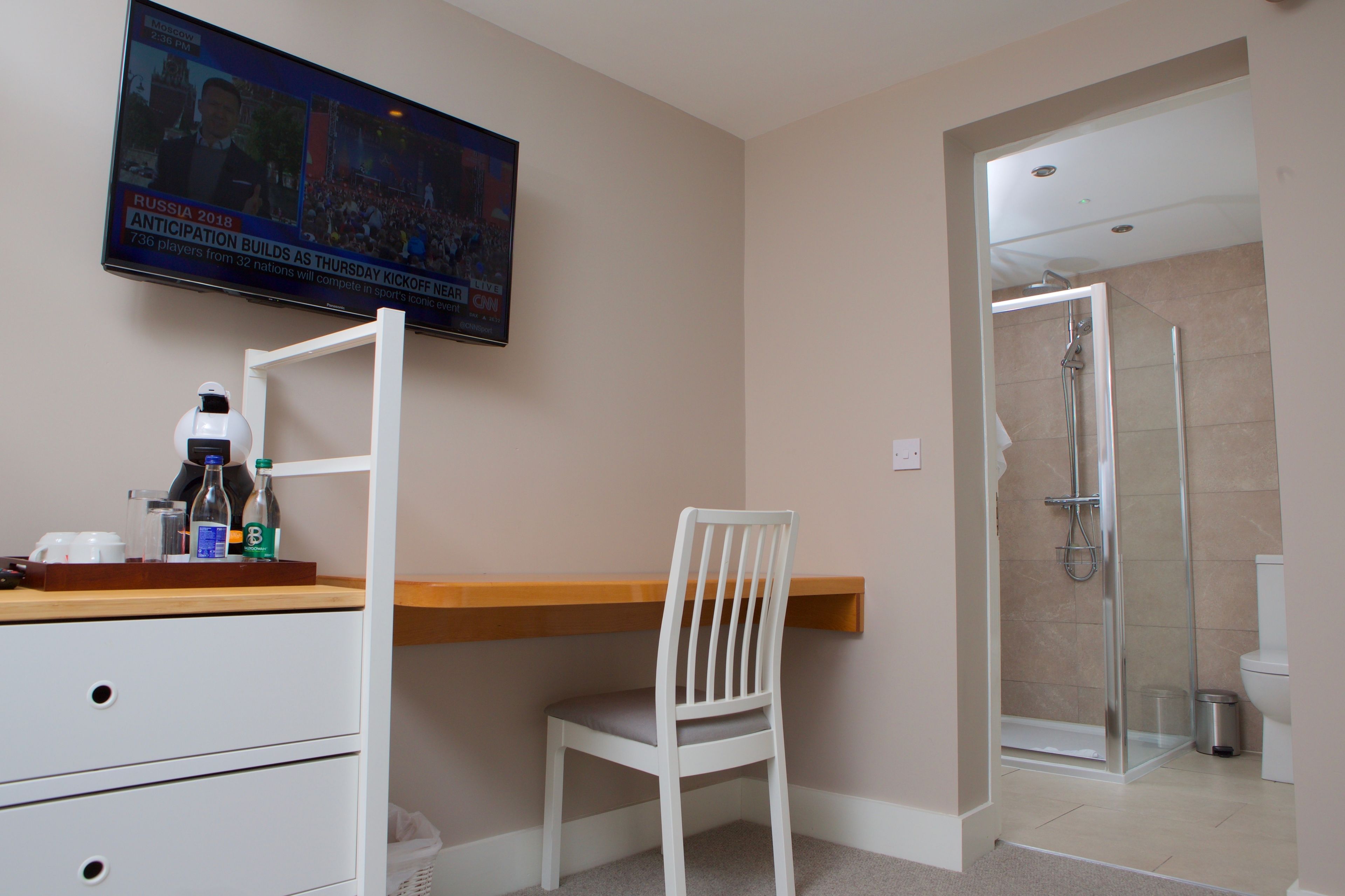 A modern bathroom with a shower, toilet, and a TV mounted on the wall displaying a sports event.