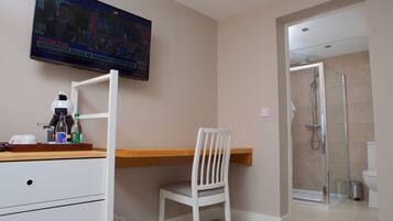 A modern bathroom with a shower, toilet, and a TV mounted on the wall displaying a sports event.