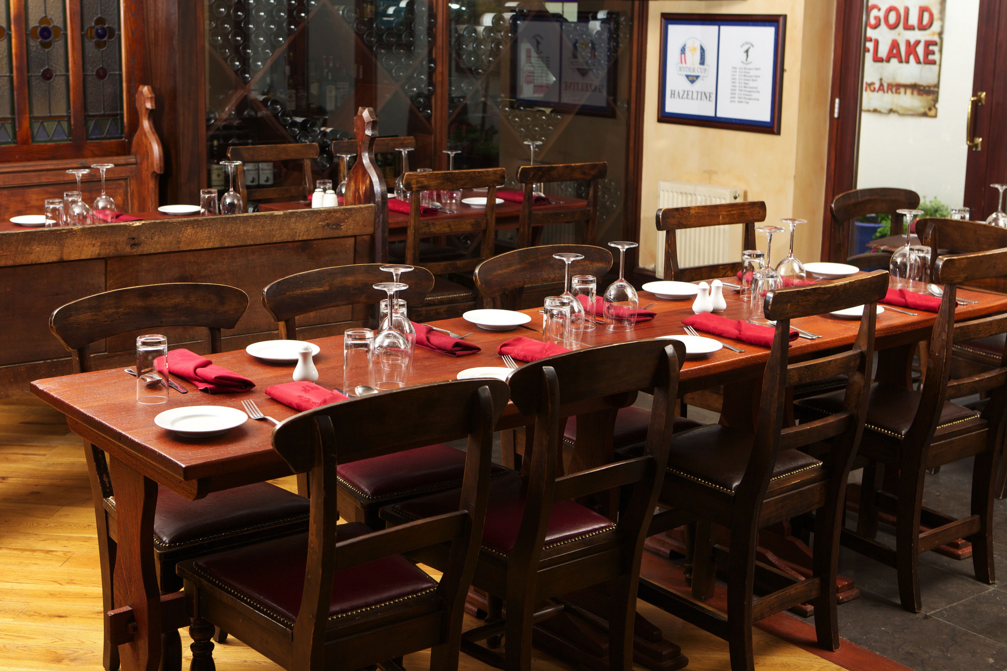 A dining area with wooden tables and chairs, equipped with wine glasses, plates, and cutlery.