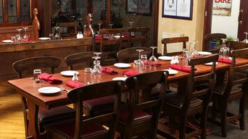 A dining area with wooden tables and chairs, equipped with wine glasses, plates, and cutlery.