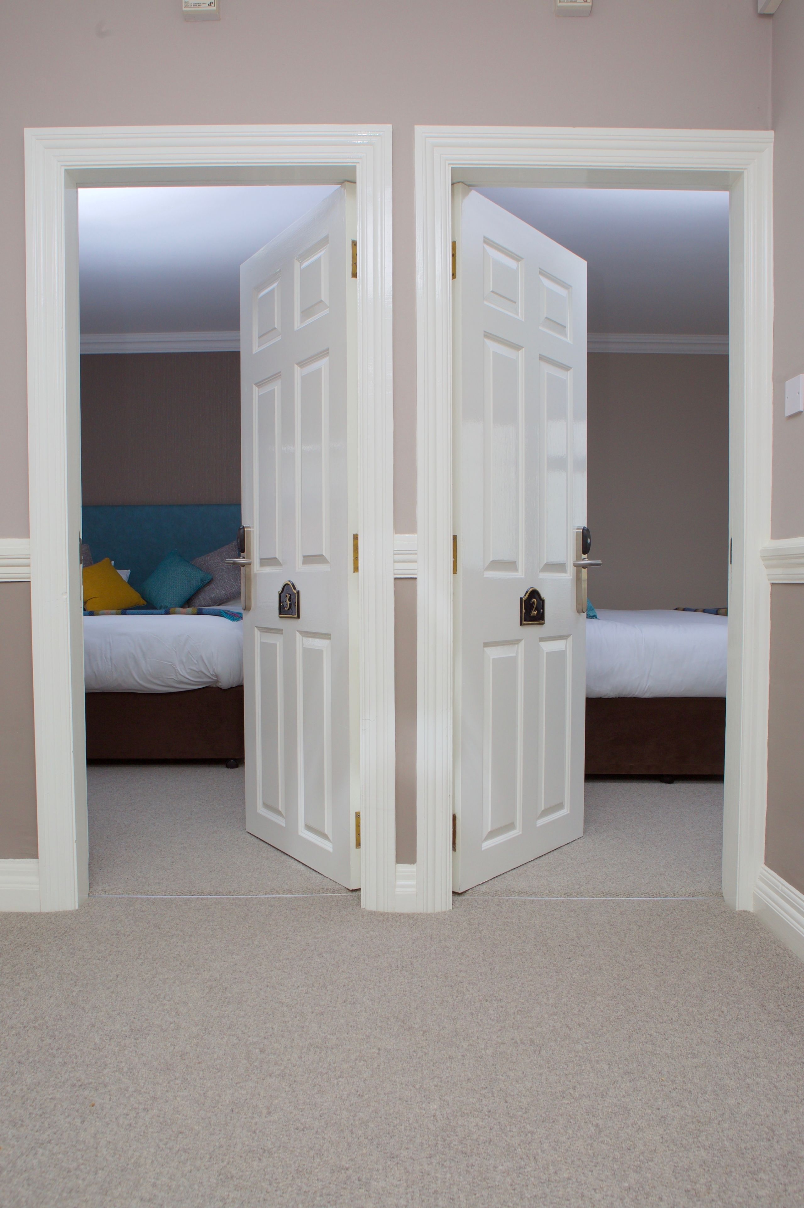 A bedroom with two beds, a door, and a carpeted floor.