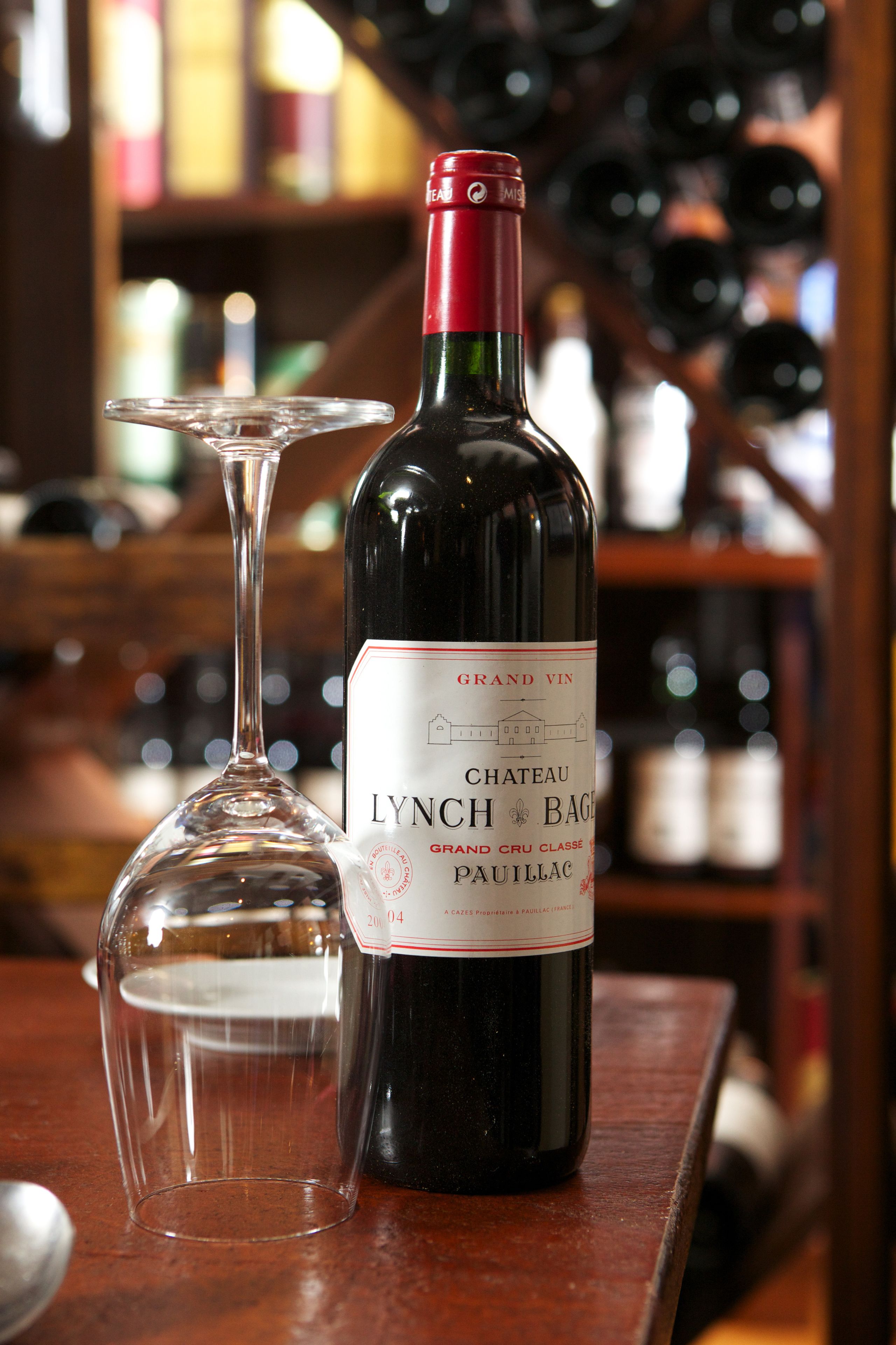 A bottle of Chateau Lynch Bages Grand Cru Classé Pauillac wine and a wine glass on a wooden surface.