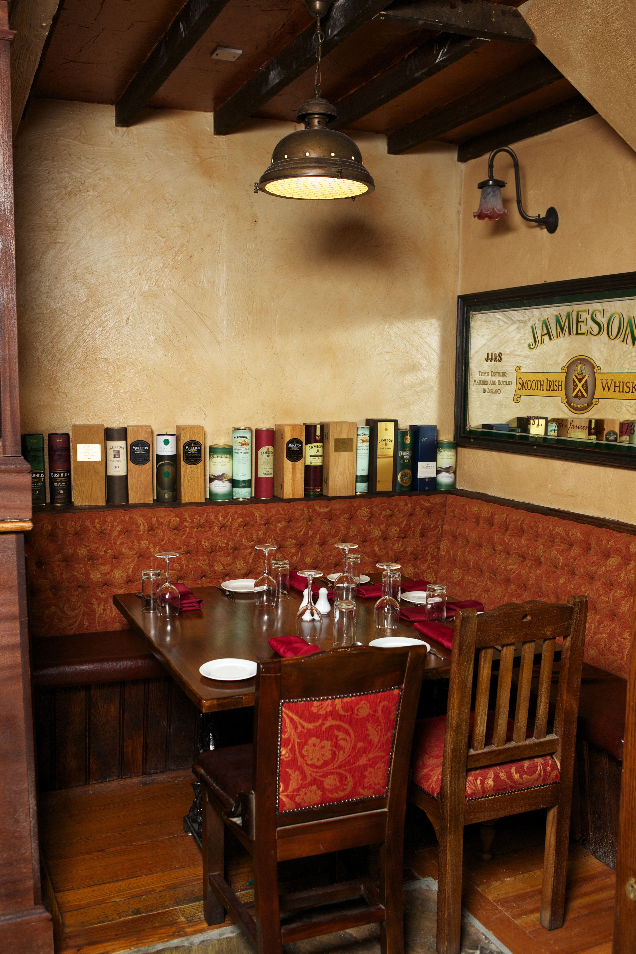 A restaurant interior with a wooden table set for dining, a bench, and a wall displaying various whiskey bottles.