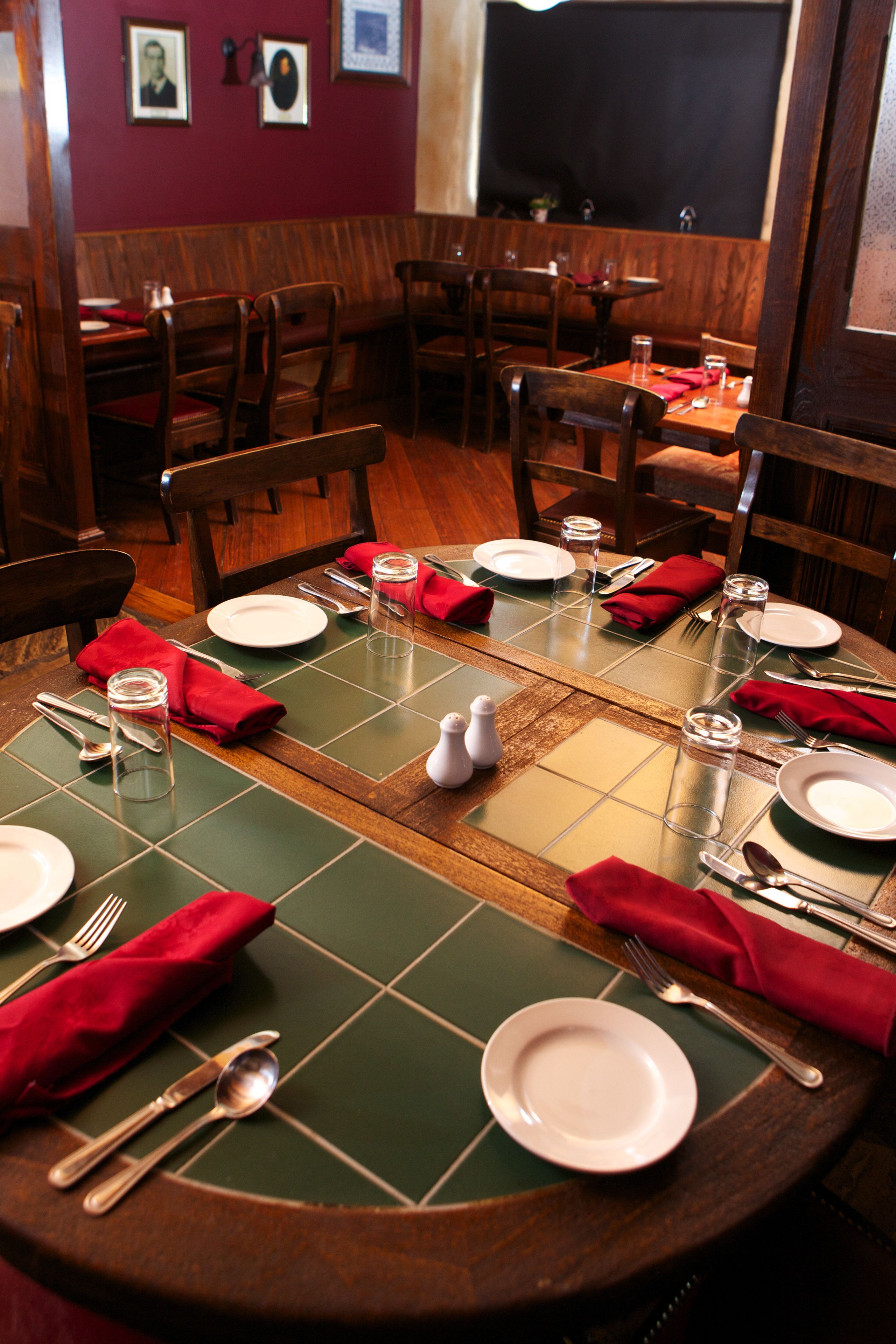 A dining area with wooden tables and chairs, green placemats, and red napkins.